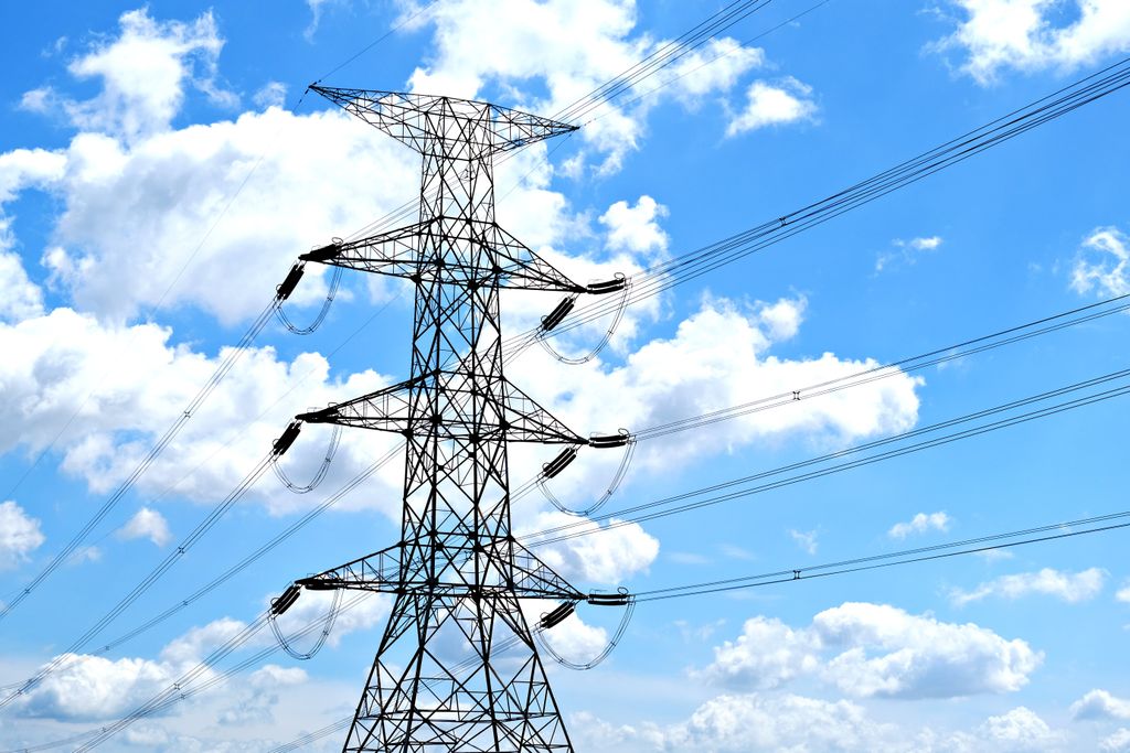 Electricity pylon with high voltage lines set against a vibrant blue sky with clouds.